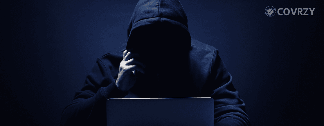 a person wearing a dark hoodie sitting infront of his laptop in a dark isolated place