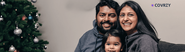 A man sitting with his wife and his child, all wearing a grey colored hoodie. A Christmas tree can be seen standing beside them