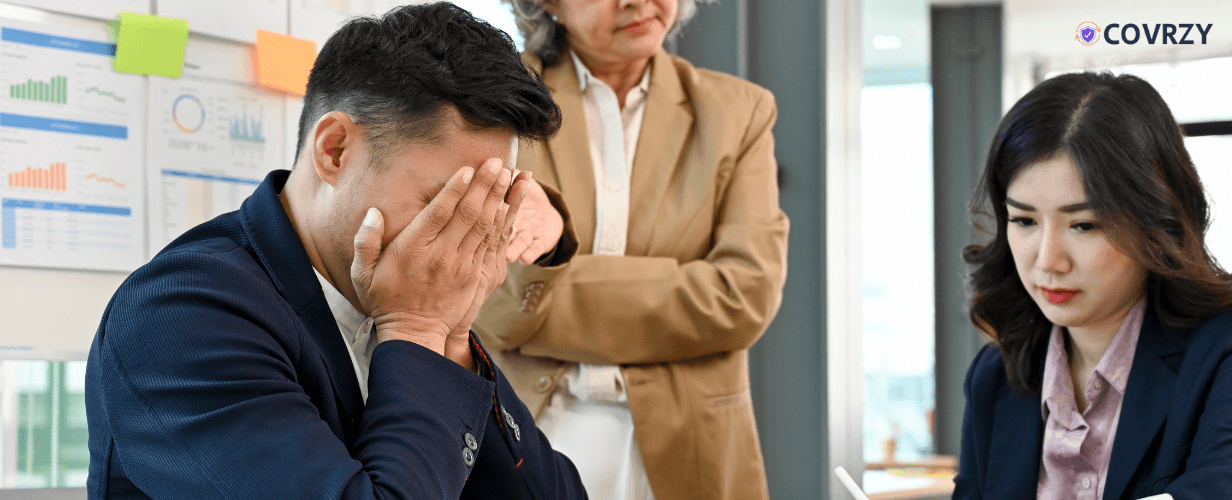 A man covering his face with his hands, two female employees present beside him